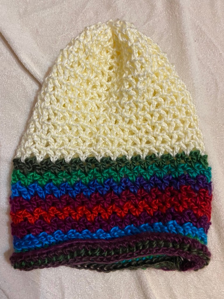 Photo of a crocheted slouch hat. The bottom half is rich blue, red, purple, and green. The top half is a yellow-white.